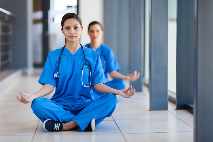 2 nurses in scrubs meditating in a hallway